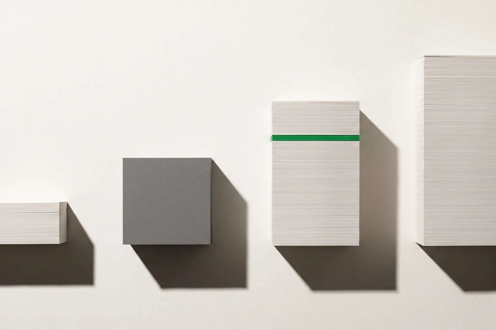 Quatre piles de papier blanc d'épaisseurs inégales vues de face, la deuxième remplacée par un bloc de carton gris, une fine tranche verte insérée dans la troisième.