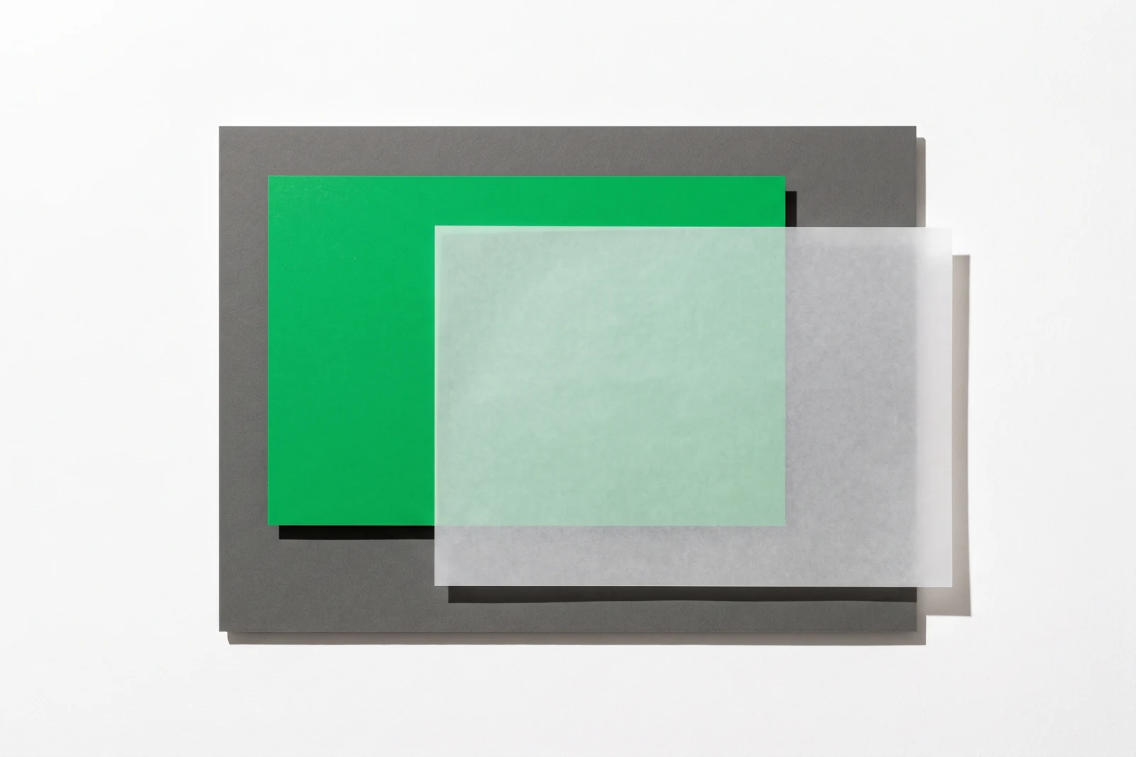 Une carte de papier vert posée sur une plaque de carton gris, à moitié recouverte par une feuille de calque décalée vers la droite.