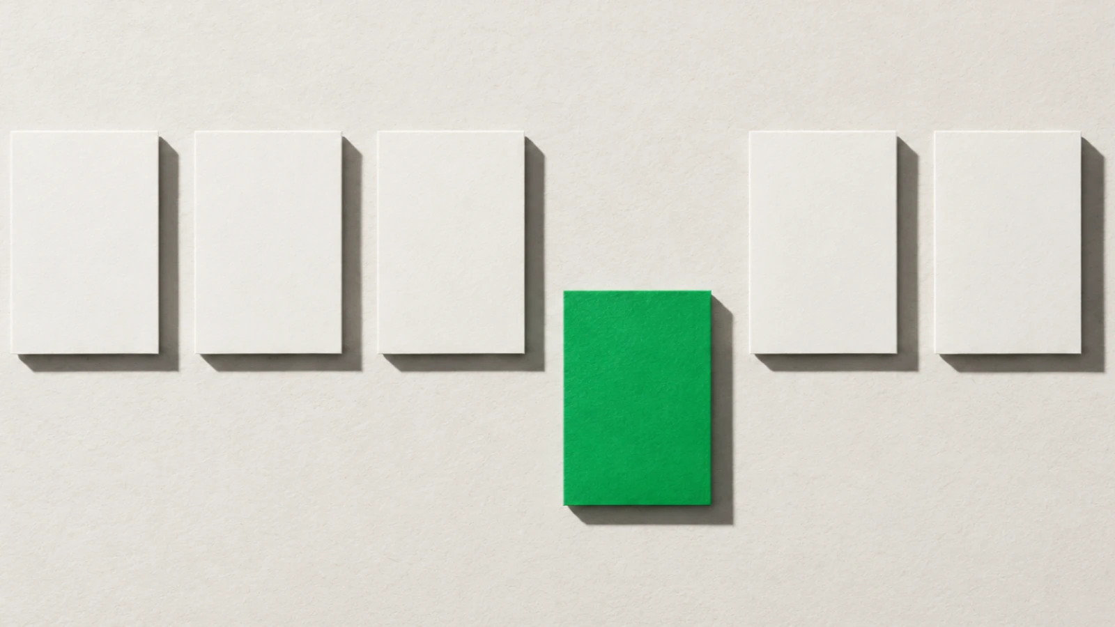 Six cartes de papier vierge alignées en rang sur un fond beige, la quatrième, verte, sortie du rang vers le bas, ombres dures projetées vers le bas à droite.
