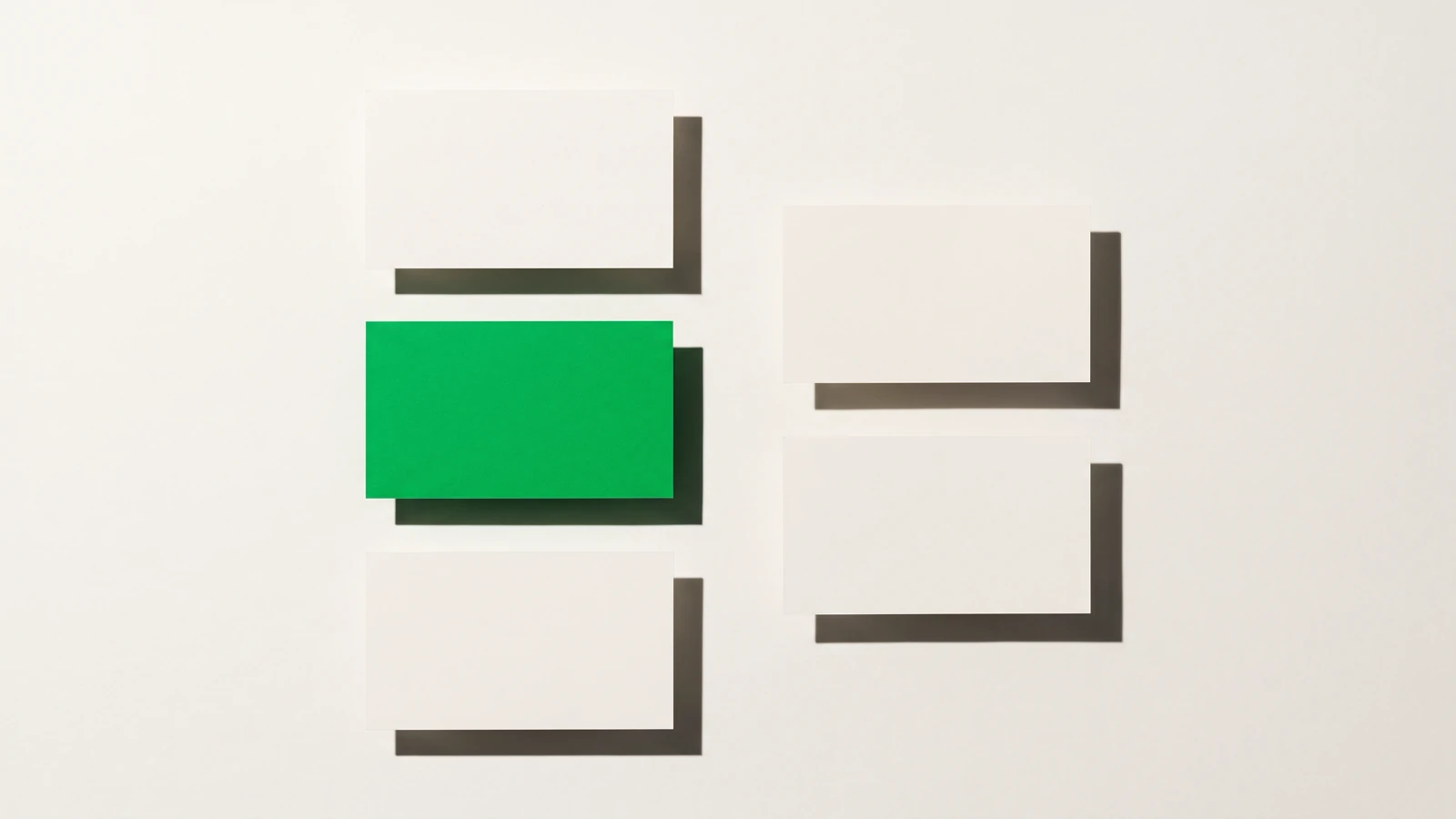 Des cartes de papier vierge triées en deux colonnes nettement séparées, ombres dures projetées vers le bas à droite.