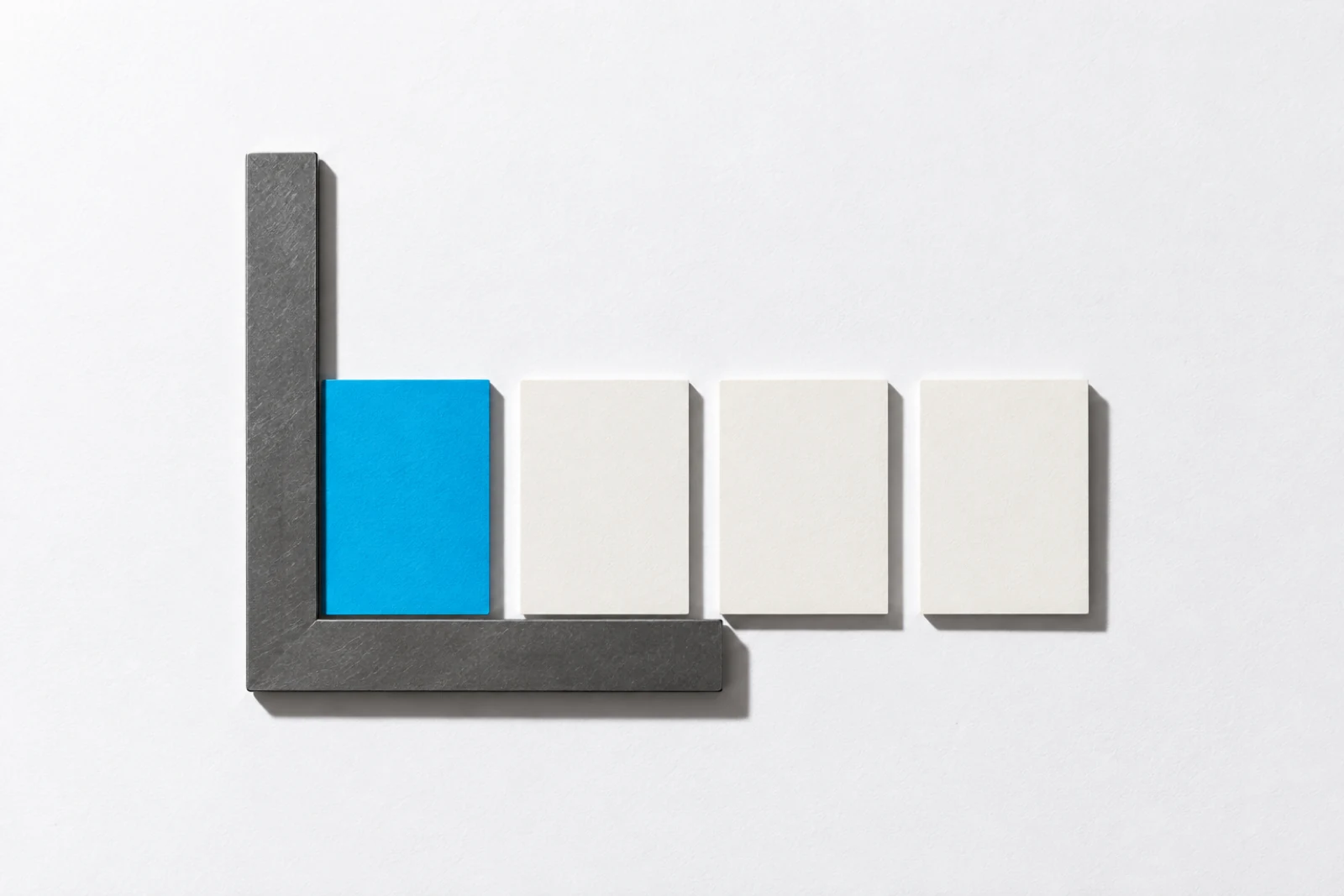 Une équerre grise en L contre laquelle s’alignent quatre cartes, la première bleue en butée dans l’angle, les trois suivantes crème