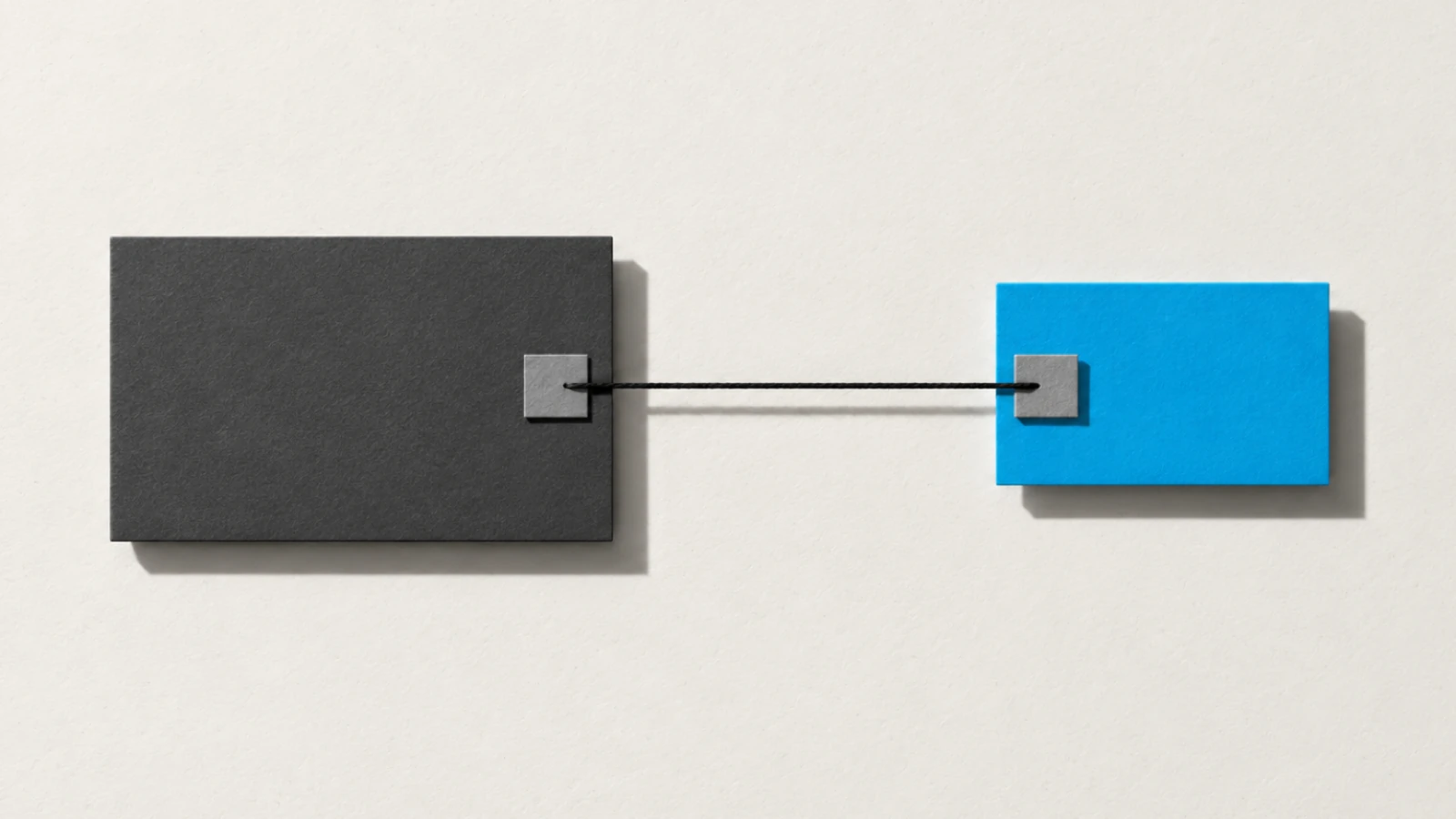 Deux cartes posées à plat sur un papier crème, une grande grise et une petite bleue, reliées par un fil noir tendu entre deux attaches carrées