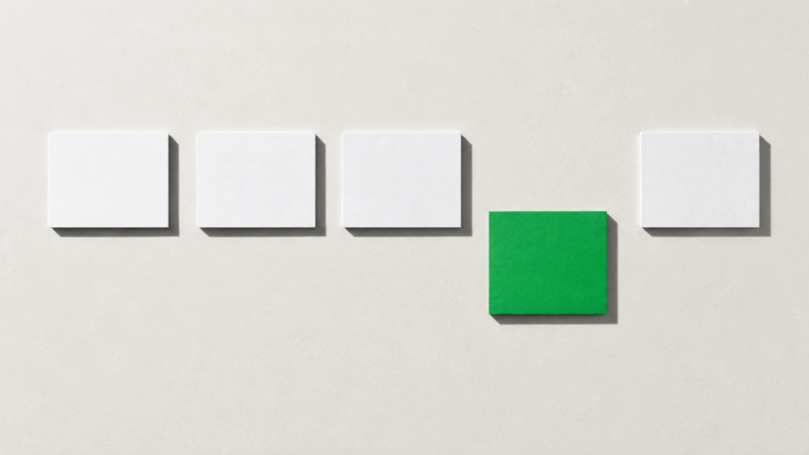 Cinq cartes blanches alignées en rangée sur un papier crème, dont la quatrième, verte, est tirée plus bas, hors de la ligne.