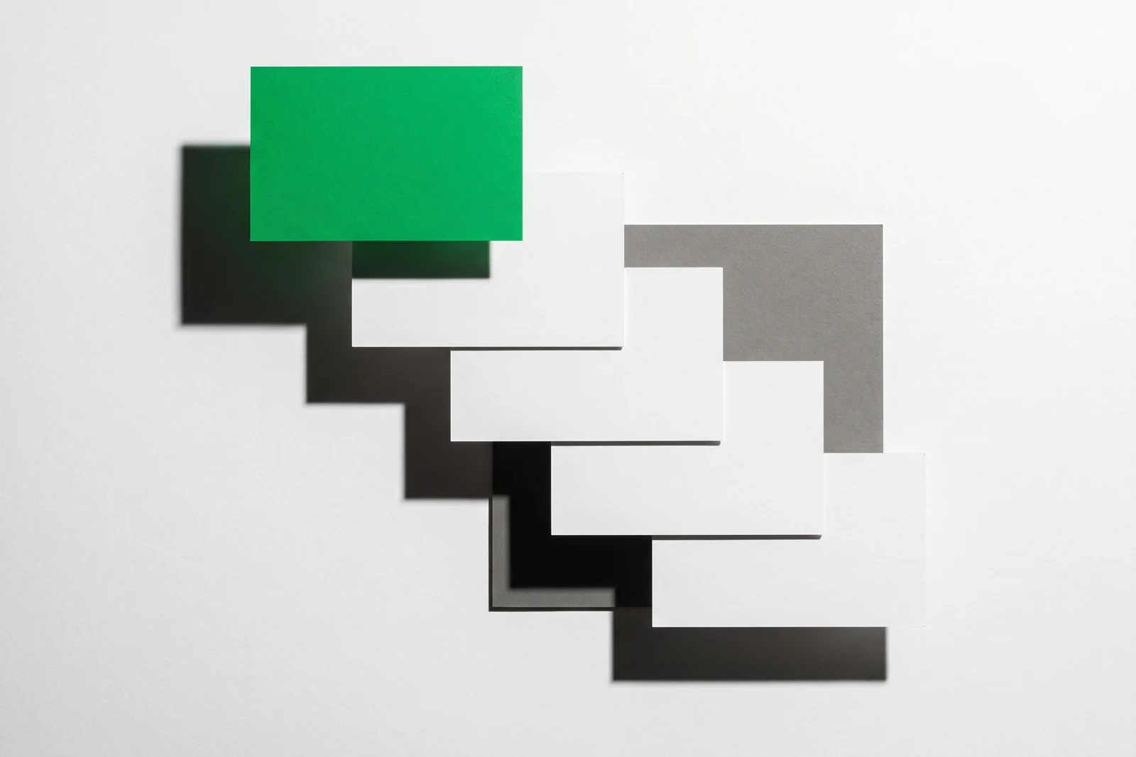 Cinq cartes de papier vierge disposées en escalier descendant, la plus haute détachée du groupe et teintée de vert, ombres nettes vers le bas à droite.