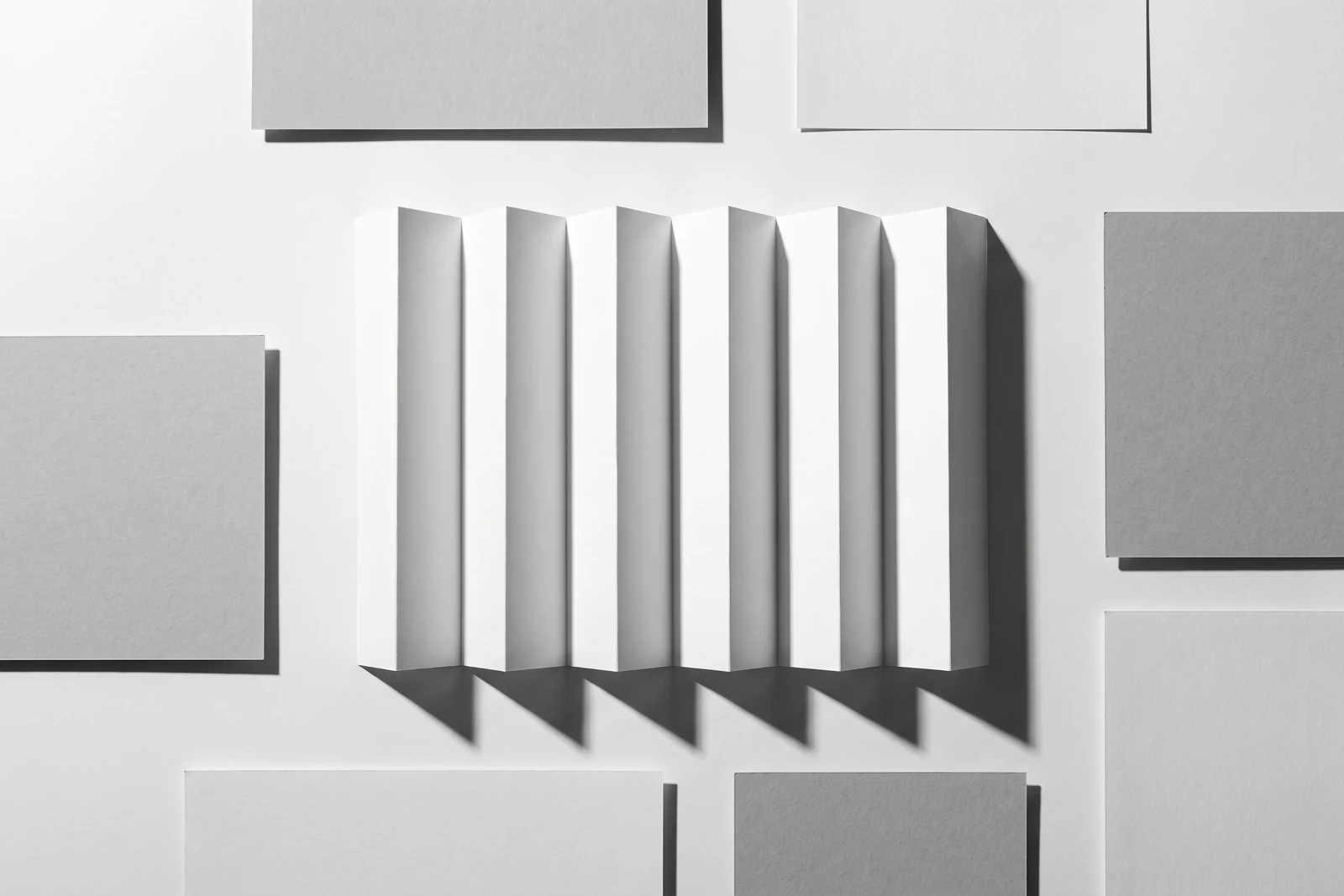 Une feuille de papier fin pliée en accordéon à arêtes vives, ombres dures projetées vers le bas à droite.