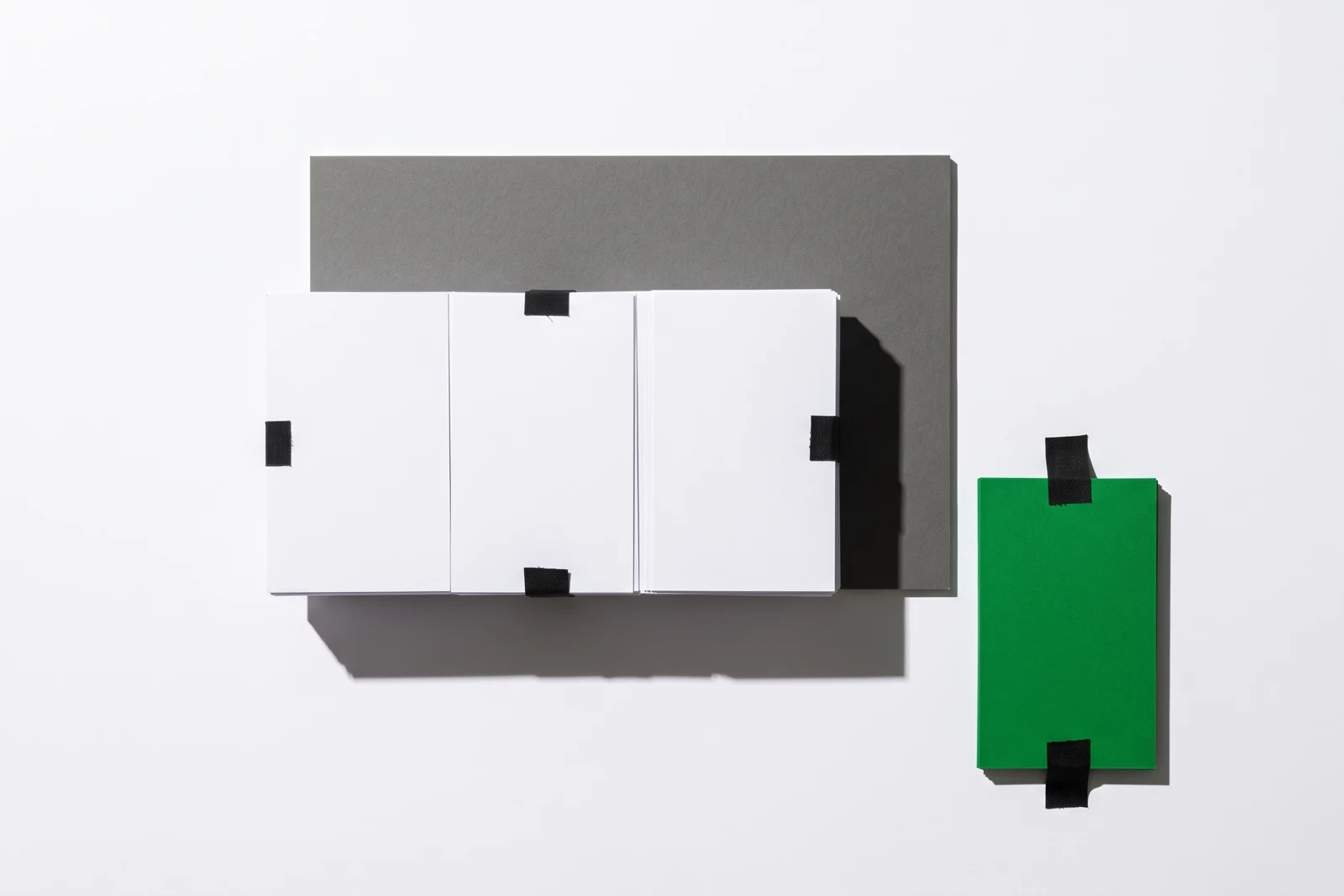 Un bloc compact de cartes de papier vierge scotché contre une surface verticale, et une carte verte tenue à l'écart du bloc, ombres dures projetées vers le bas à droite.