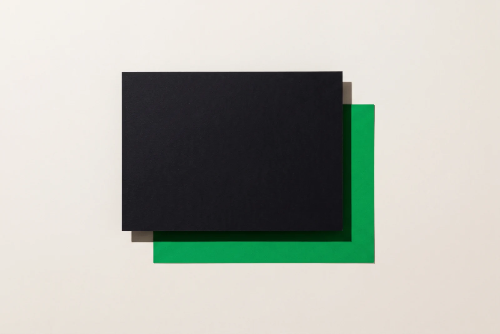 Une grande carte de papier noir posée sur une feuille verte et décalée vers le haut à gauche, ne laissant visible qu'une bande verte en L sur la droite et le bas, fond papier blanc cassé, une seule ombre nette
