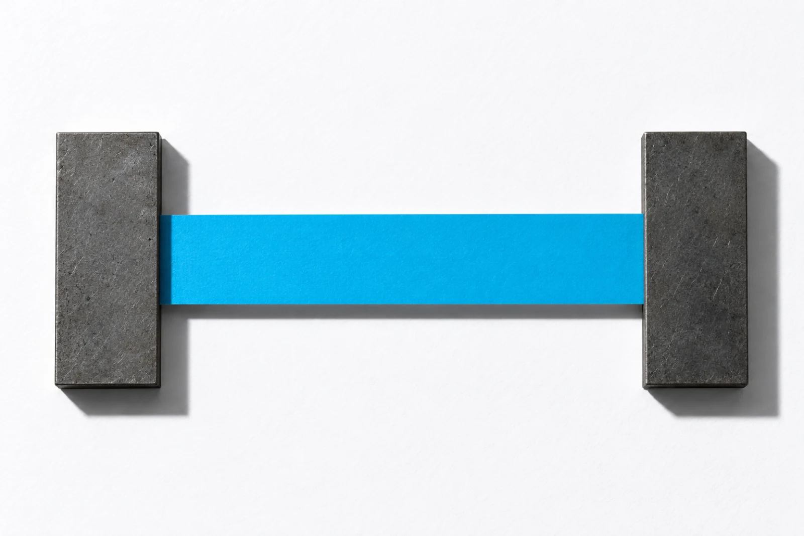Une bande de papier cyan tendue à l'horizontale entre deux plaques d'acier mat posées à plat sur un fond blanc, ombres dures vers le bas à droite.