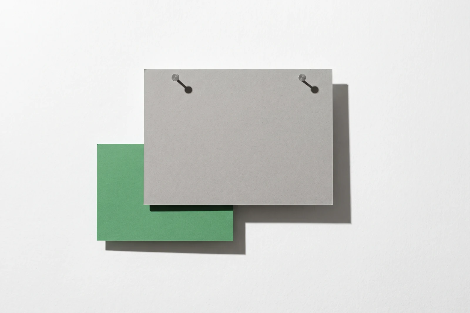 Une carte de papier vert glissée sous une plaque de carton gris punaisée, un tiers du vert dépassant du bord.