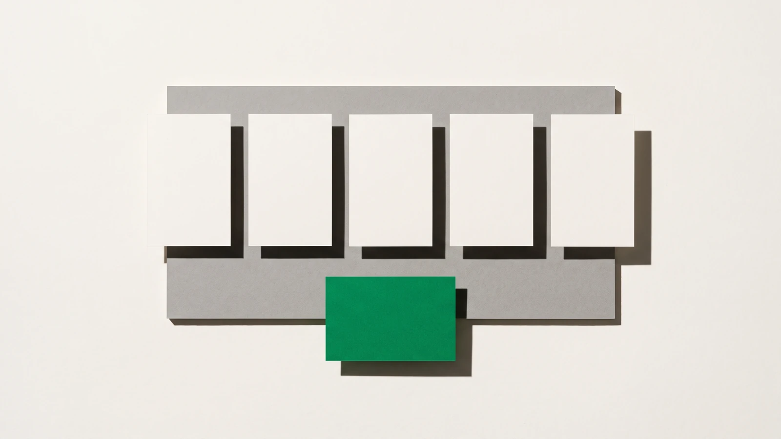 Cinq cartes de papier blanc alignées sur une plaque de carton gris, une sixième carte verte posée à l’écart sous la rangée.