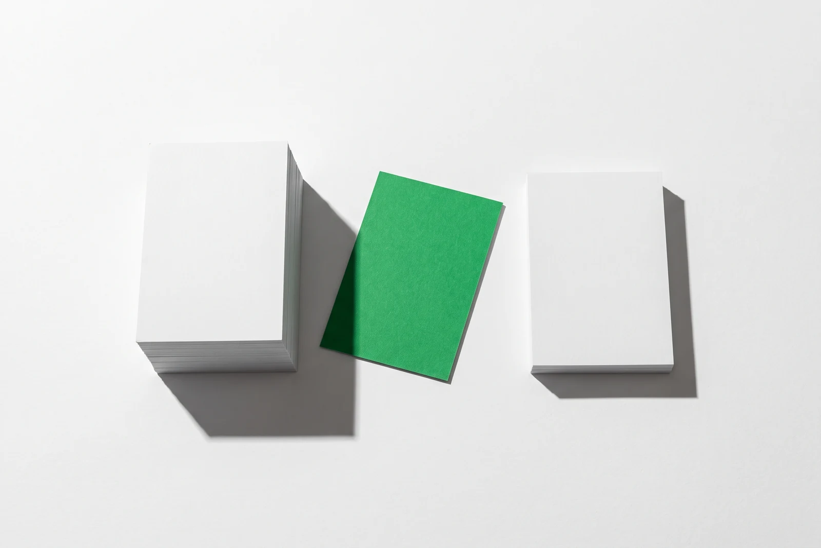 Deux piles de papier vierge d’épaisseurs très inégales, séparées par un écart où repose une carte teintée en vert.
