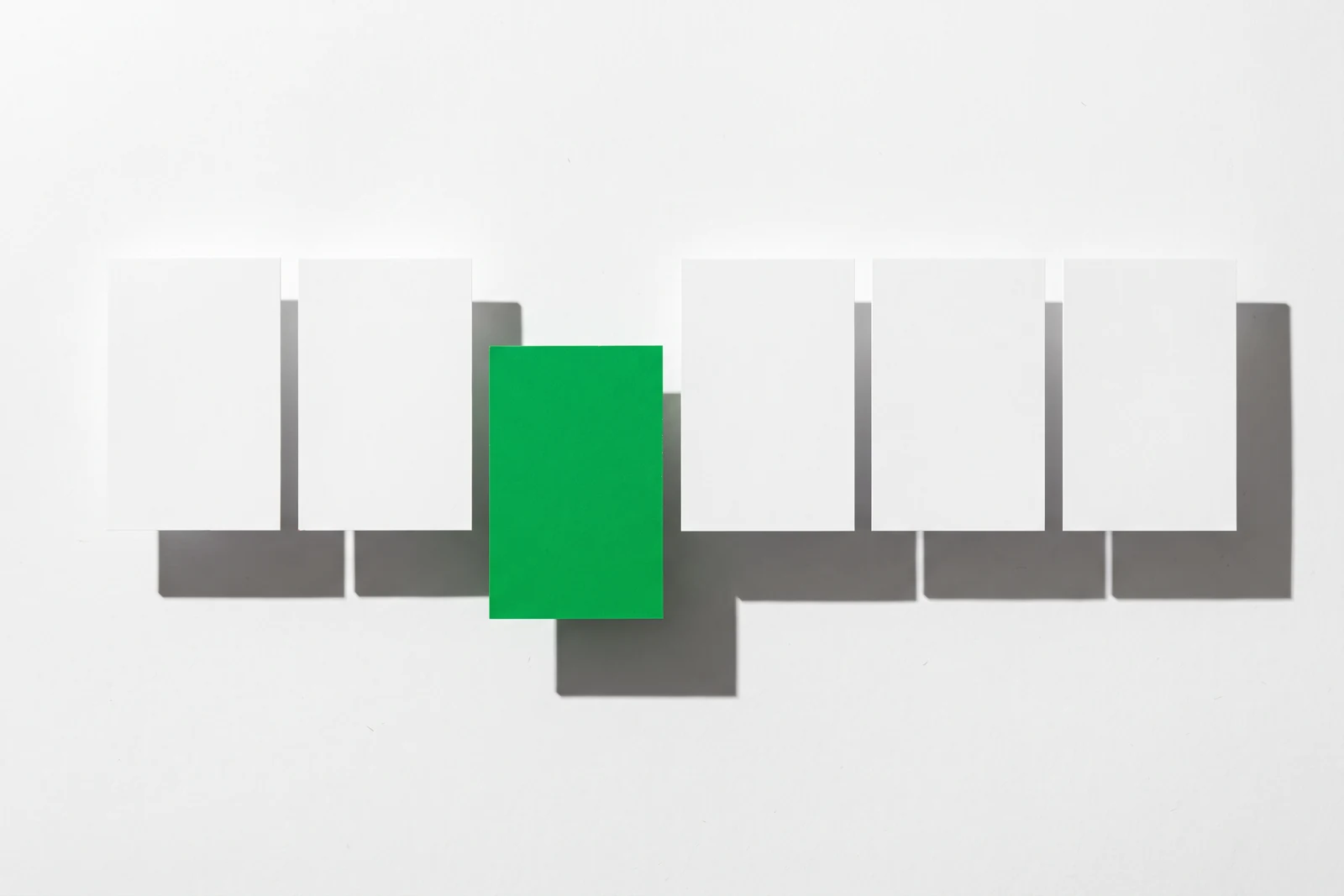 Six cartes de papier vierge alignées sur une rangée, celle du milieu teintée en vert et poussée hors de l’alignement.
