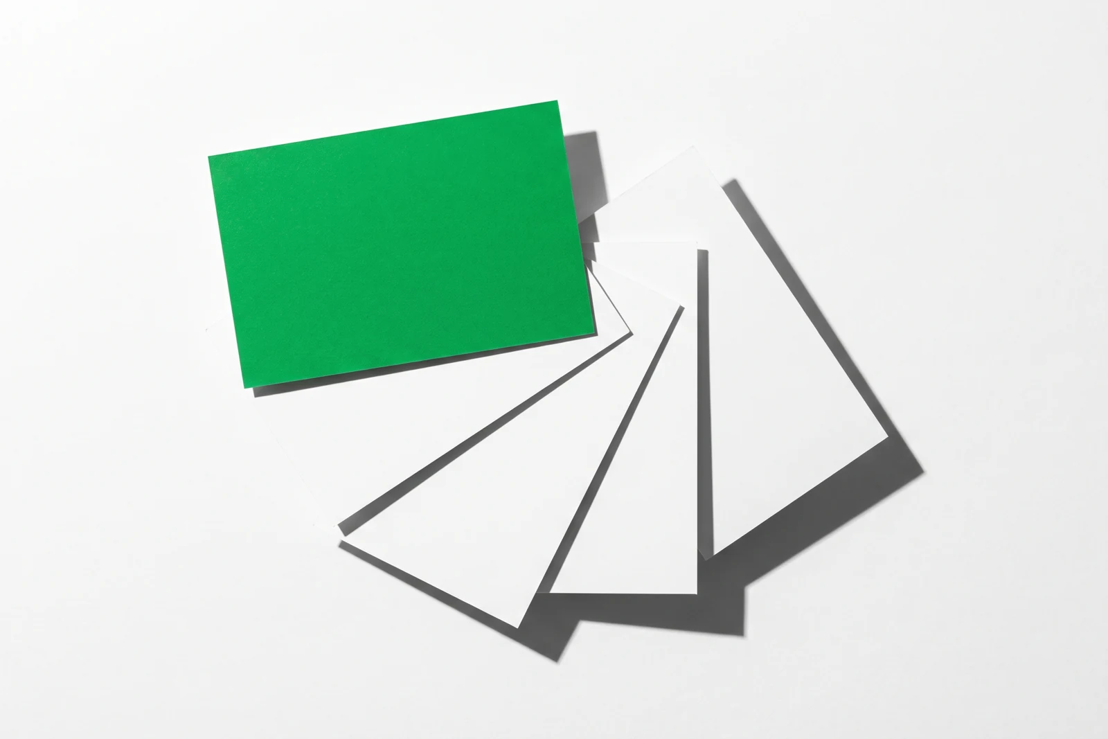 Cinq cartes de papier vierge qui se recouvrent en éventail, celle du dessus teintée en vert et entièrement dégagée.