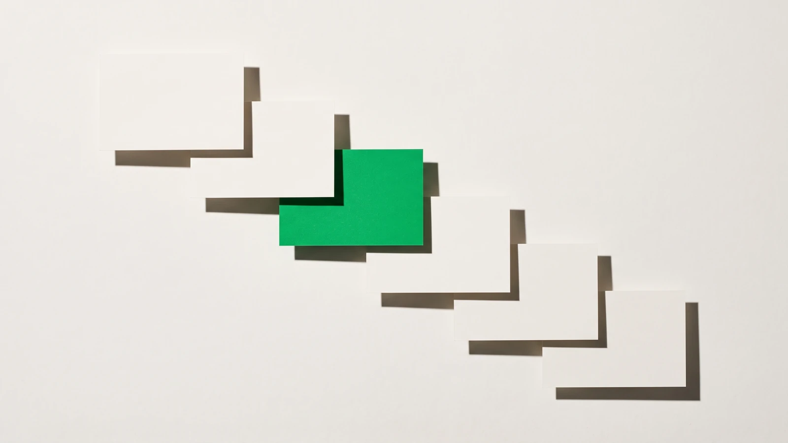 Six cartes de papier vierge disposées en escalier descendant de gauche à droite, la troisième teintée en vert.
