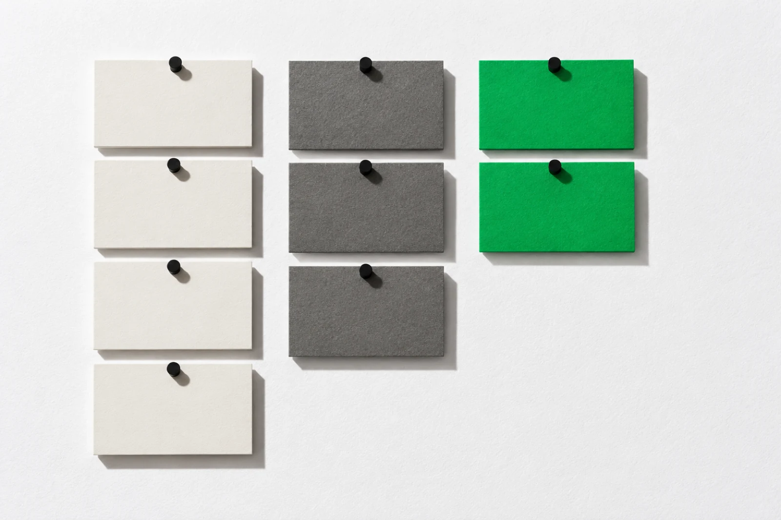 Trois colonnes de cartes épinglées sur un mur blanc : quatre cartes blanches, trois cartes grises, deux cartes vertes, ombres nettes vers le bas à droite.