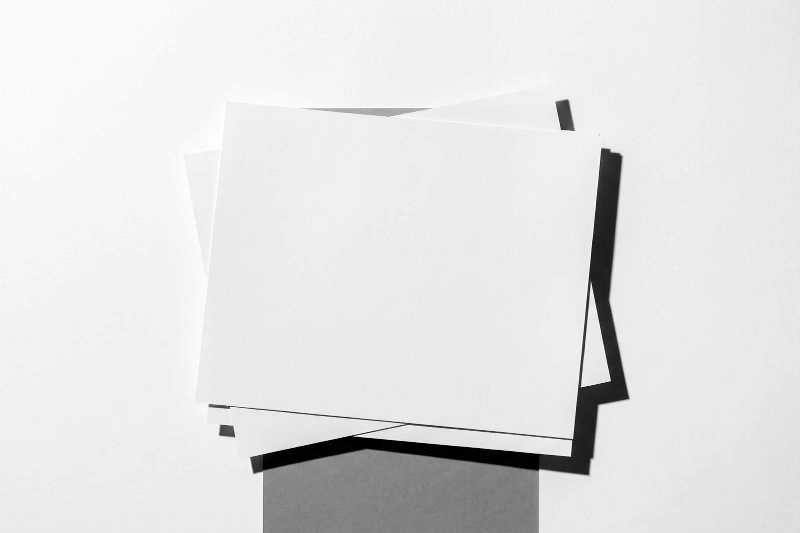 Des feuilles de papier fin empilées à plat et visiblement désalignées, ombres dures projetées vers le bas à droite.
