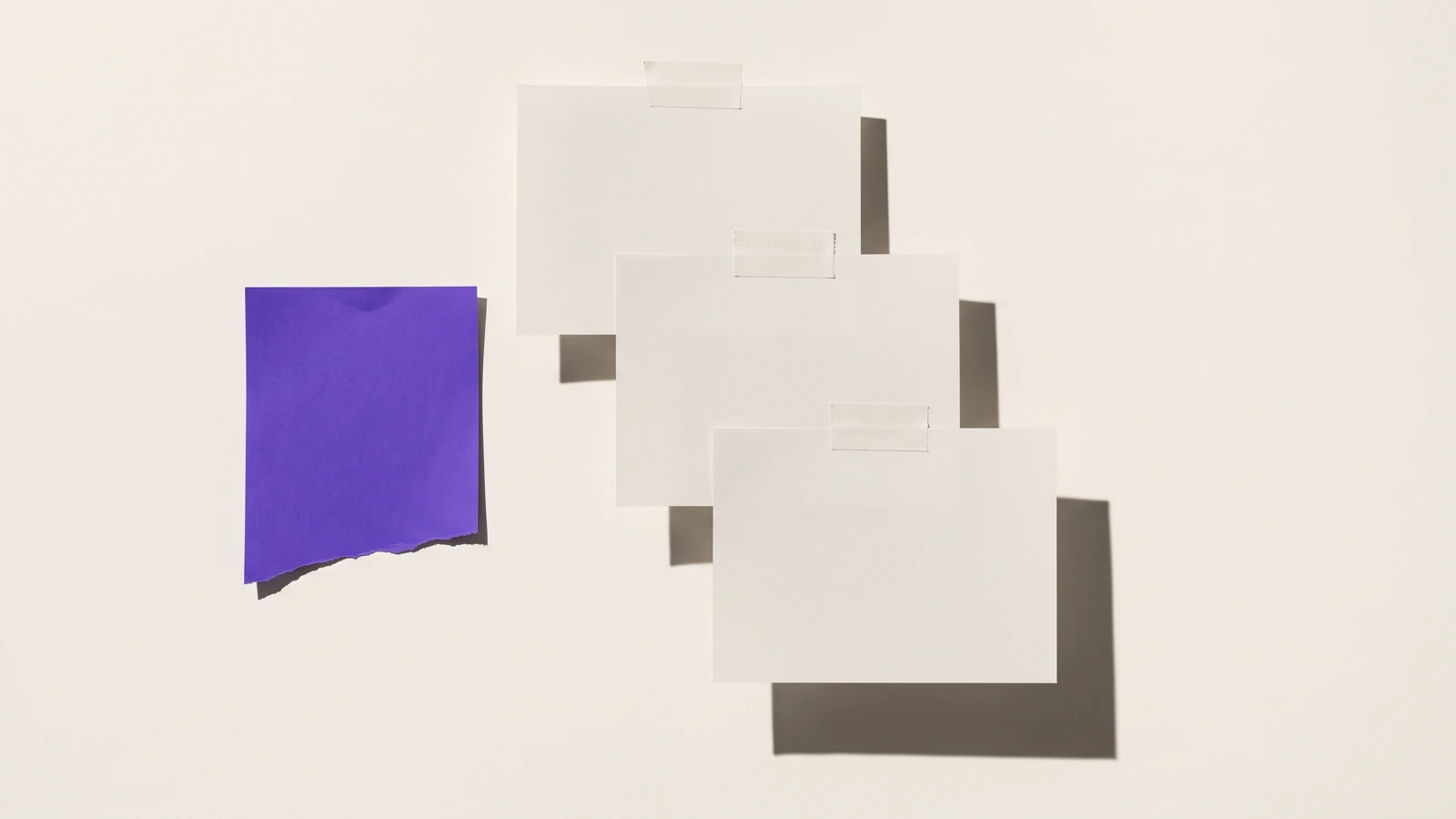 Des feuilles de papier fin collées en couches qui se recouvrent partiellement, ombres dures projetées vers le bas à droite.