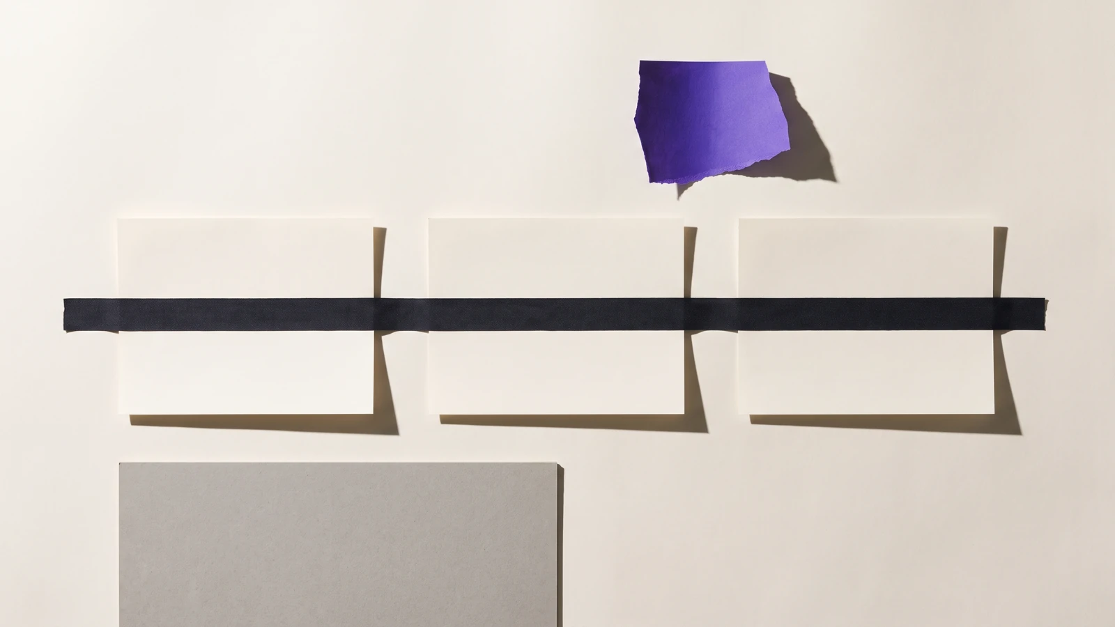 Des feuilles de papier scotchées à plat, le coin de la feuille du dessus arraché, ombres dures projetées vers le bas à droite.