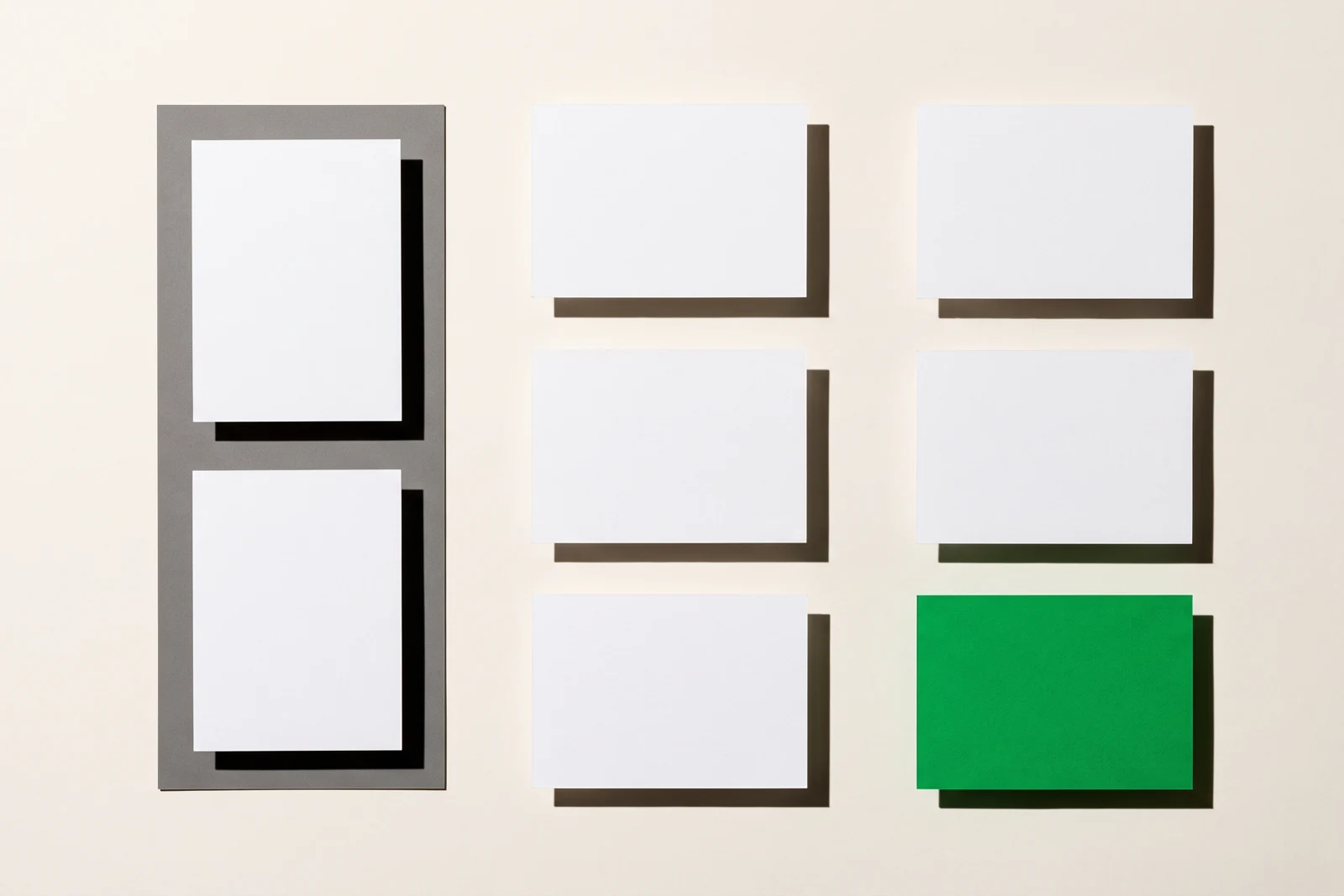Neuf cartes de papier vierge triées en trois colonnes de hauteurs inégales, la carte du bas de la colonne de droite en papier vert, ombres dures projetées vers le bas à droite