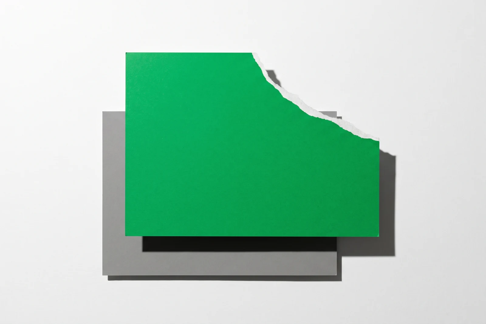 Une grande carte de papier vert posée sur une plaque de carton gris, son coin supérieur droit arraché en laissant voir la fibre blanche du papier