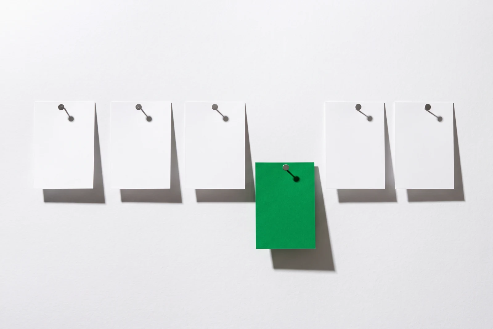 Six fiches blanches punaisées en ligne sur un mur clair, la quatrième est verte et décalée vers le bas.