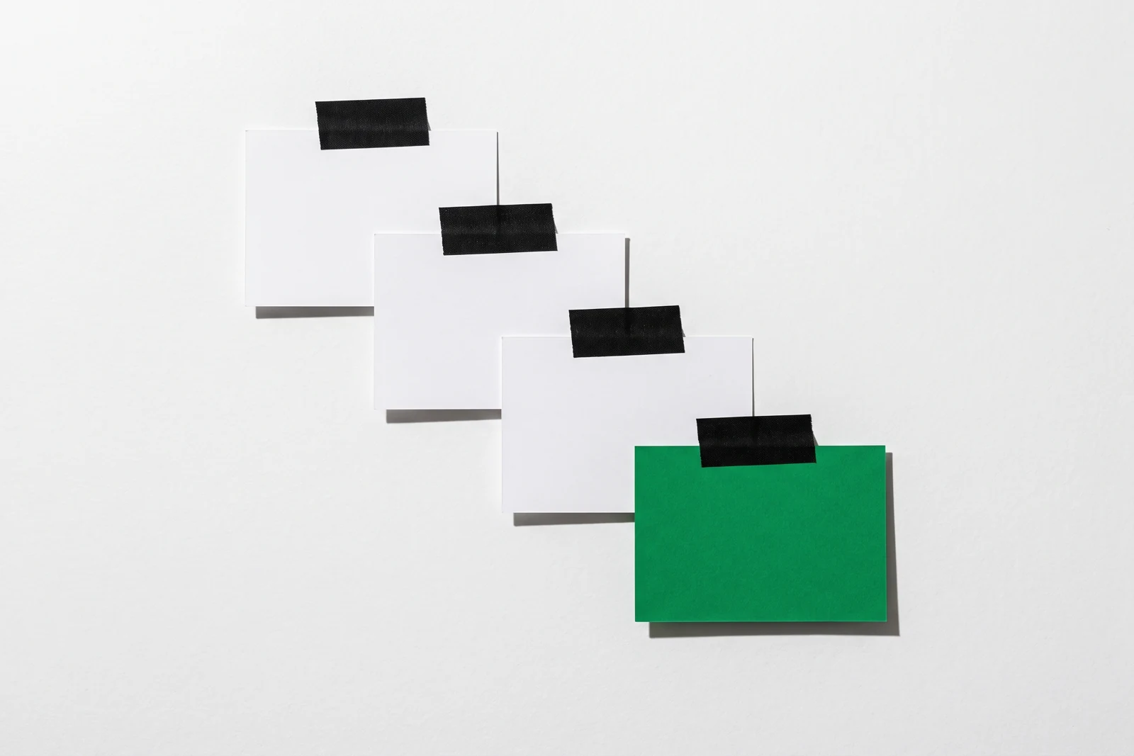 Quatre cartes fixées au ruban adhésif en escalier descendant, les trois premières blanches, la dernière verte et plus grande.