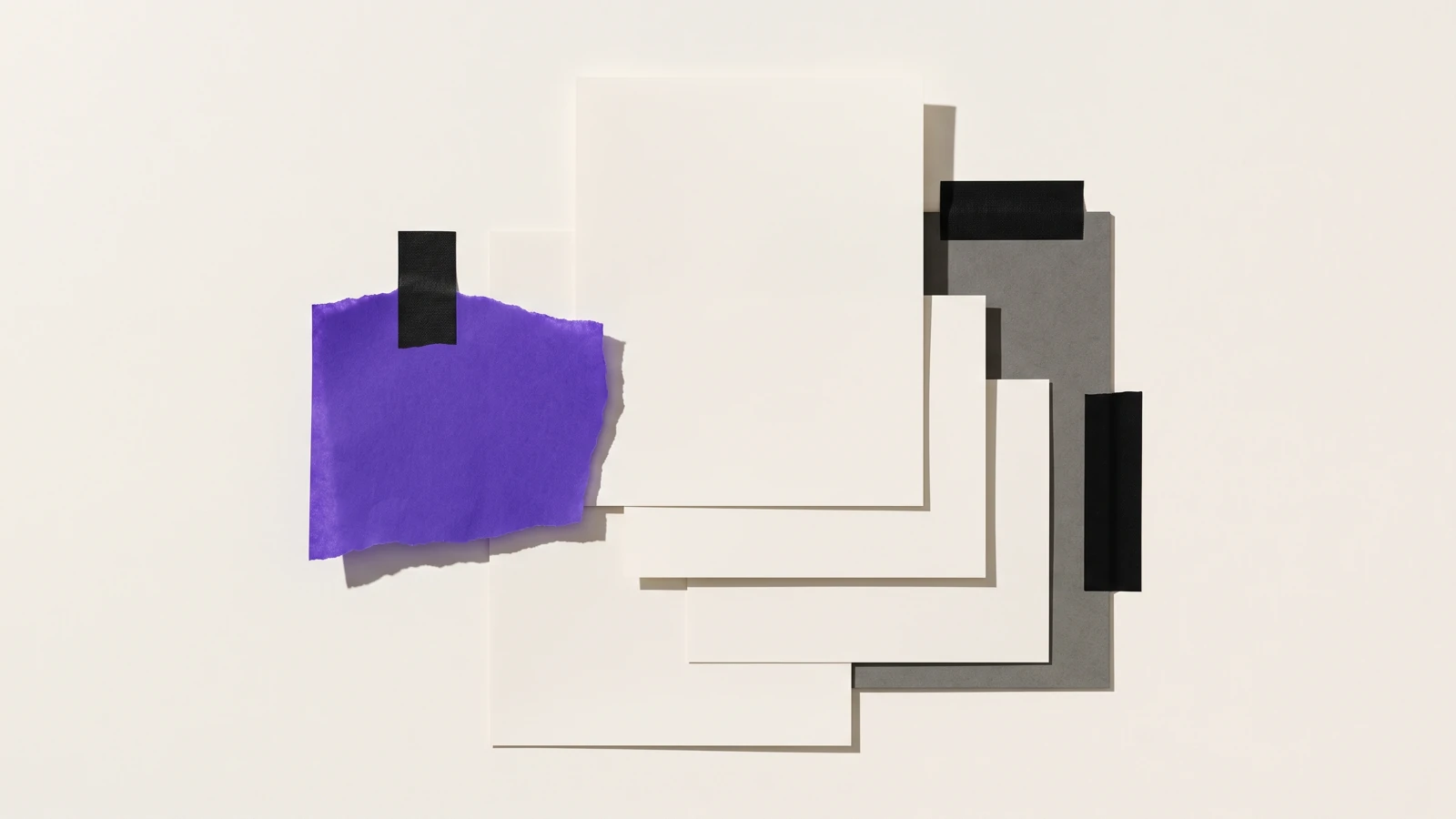 Des feuilles séparées maintenues ensemble par une seule bande de ruban toile, ombres dures projetées vers le bas à droite.
