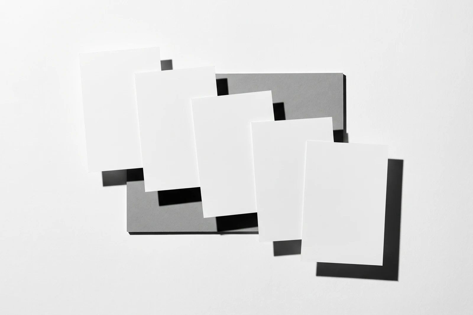 Une rangée de cartes de papier qui dérive progressivement hors de l’axe, ombres dures projetées vers le bas à droite.