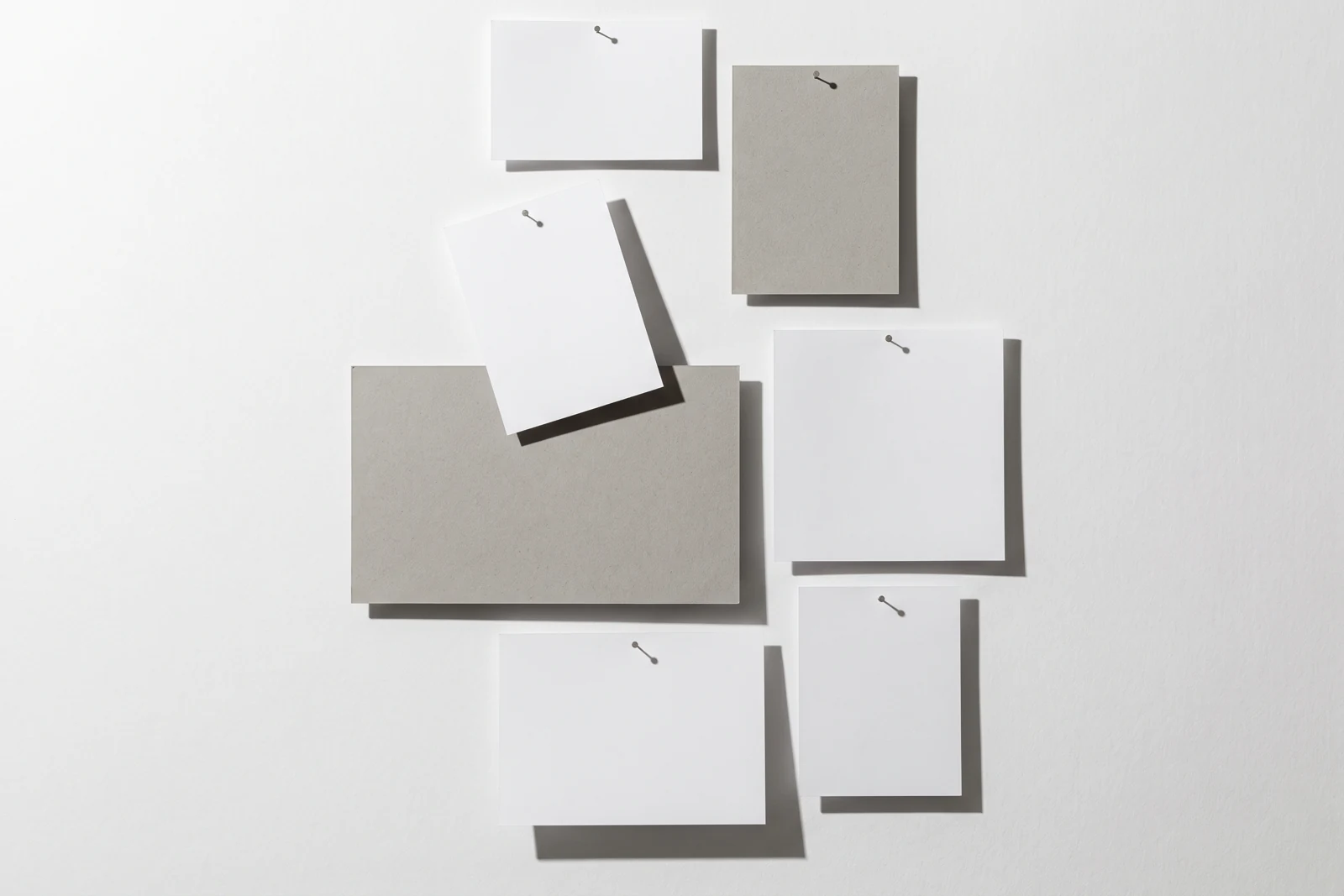 Une carte de papier en équilibre sur le bord d’une plaque de carton gris, ombres dures projetées vers le bas à droite.