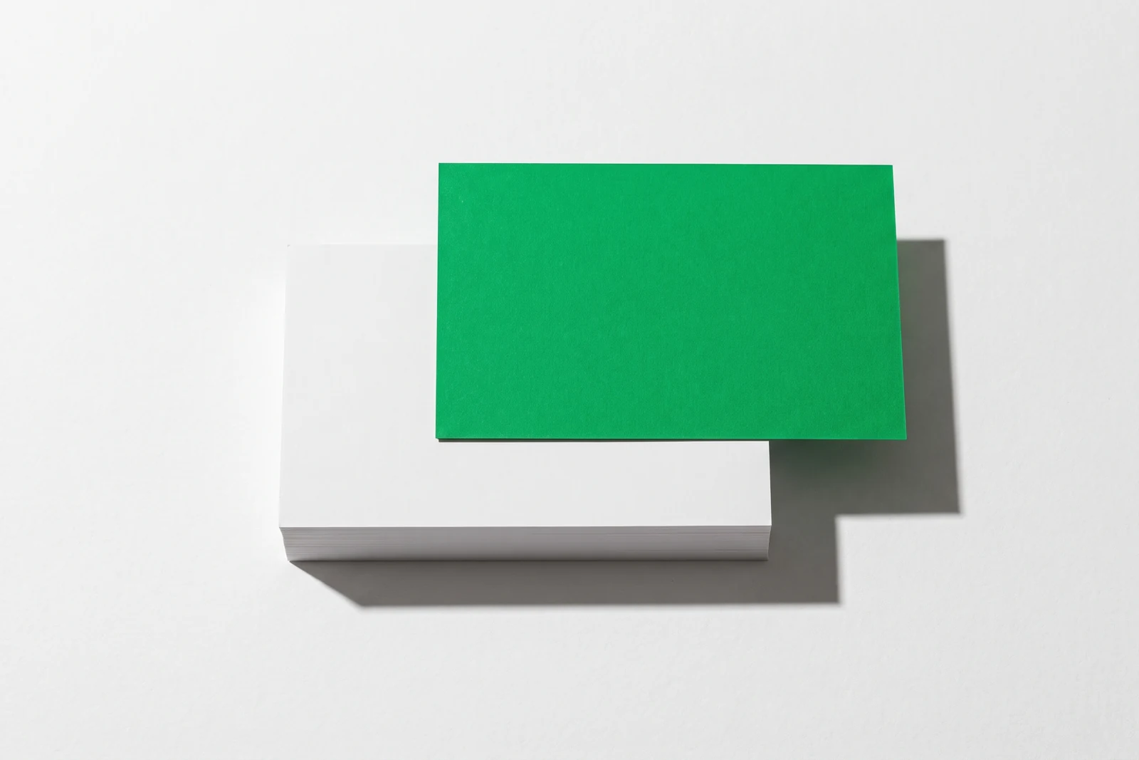 Une pile épaisse de cartes de papier blanc vue du dessus, dont la carte verte du dessus est poussée sur le côté et dépasse du bord de la pile, une seule ombre nette