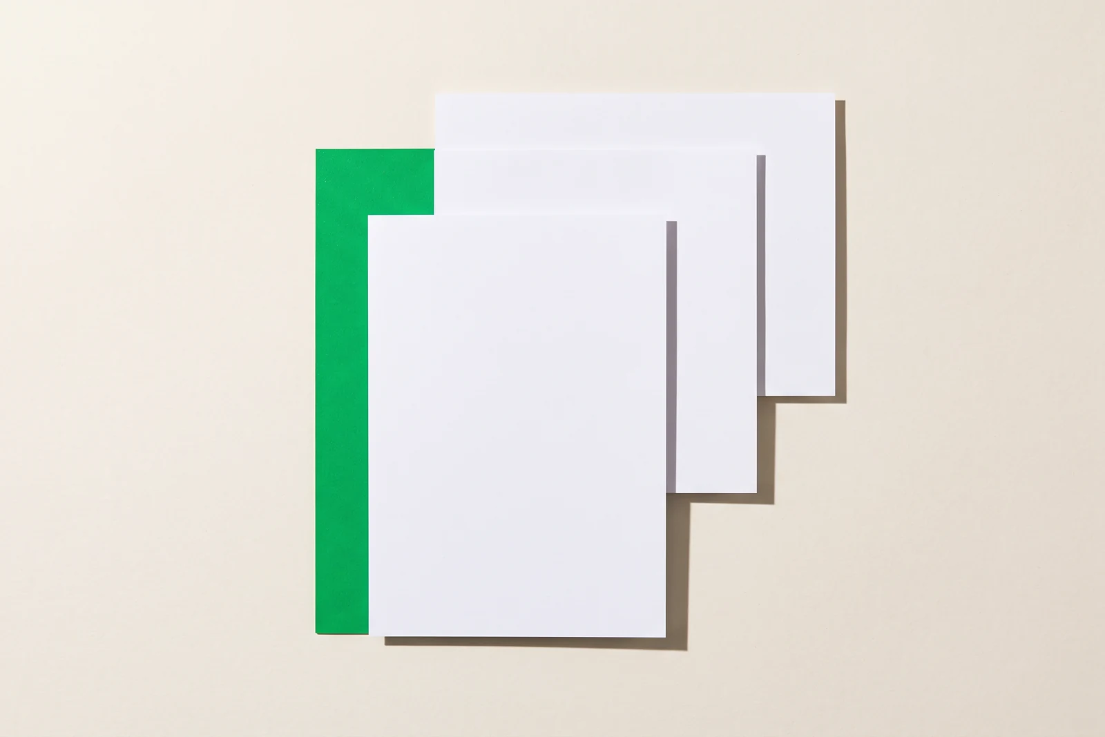 Trois feuilles blanches posées en couches décalées sur un fond crème, une feuille verte glissée dessous dont seule une bande dépasse à gauche.