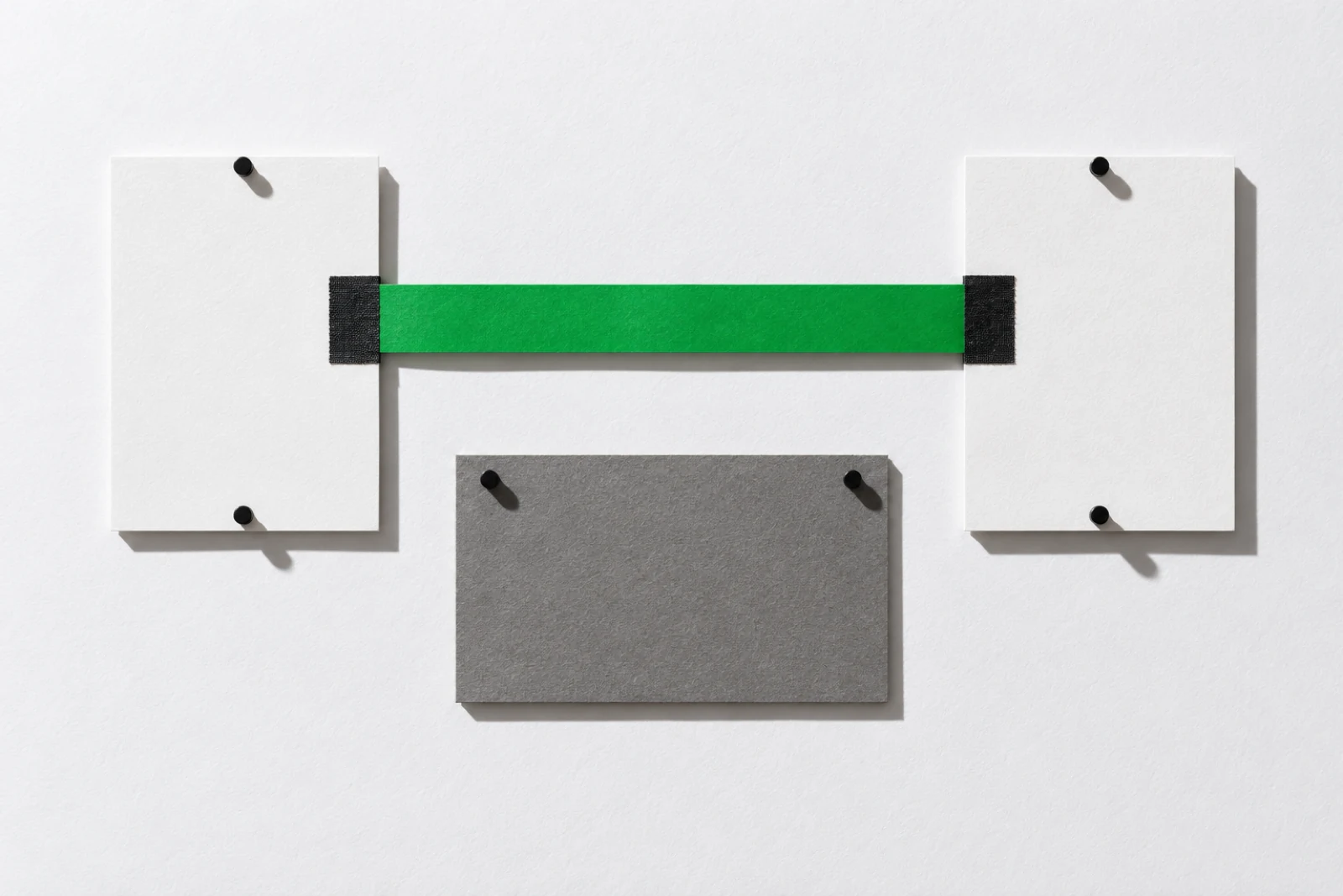 Deux cartes blanches punaisées de part et d'autre, reliées par une bande de papier vert tendue droite, au-dessus d'un carton gris punaisé.