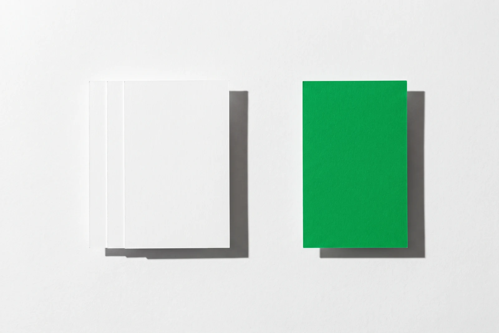 Un groupe serré de cartes de papier vierge et une carte isolée à l’écart, ombres dures projetées vers le bas à droite.