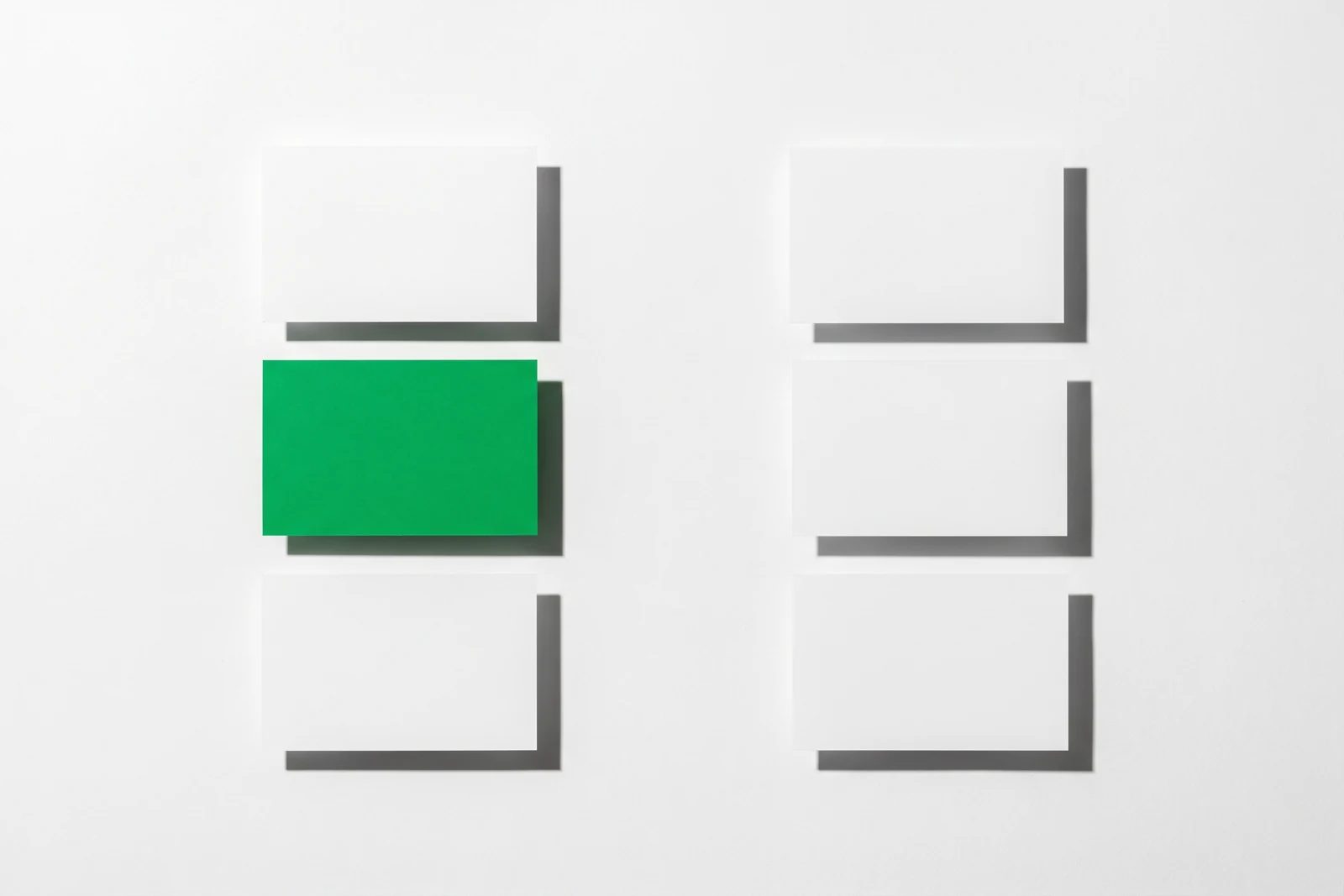 Des cartes de papier vierge triées en deux colonnes nettement séparées, ombres dures projetées vers le bas à droite.