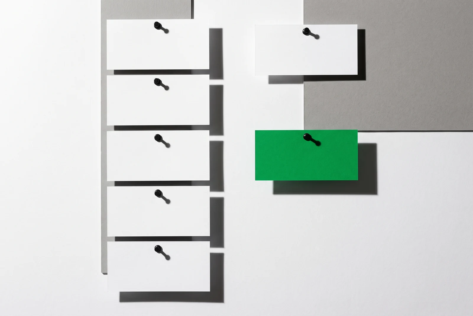 Des cartes de papier vierge triées en deux colonnes nettement séparées, ombres dures projetées vers le bas à droite.
