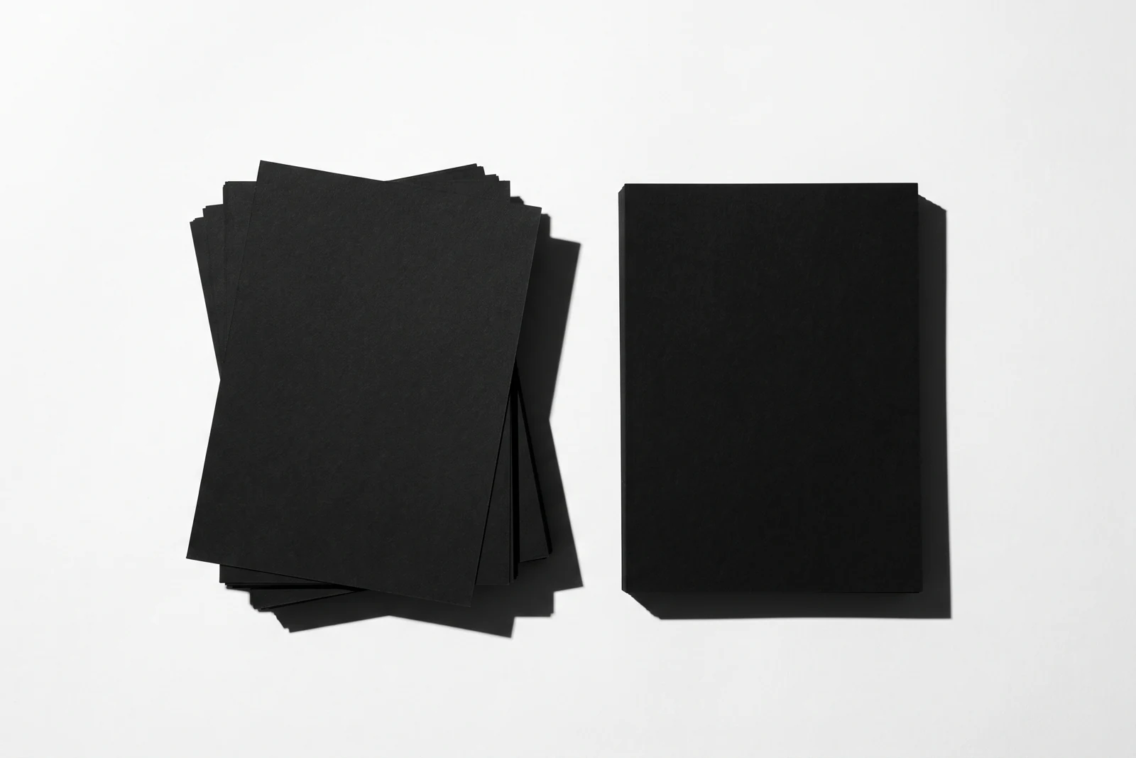 Vue de dessus, sur un fond blanc, deux piles de feuilles de papier noir mat de même hauteur, posées côte à côte : celle de gauche aux feuilles nettement désalignées, celle de droite parfaitement d’équerre ; ombres dures vers le bas à droite.