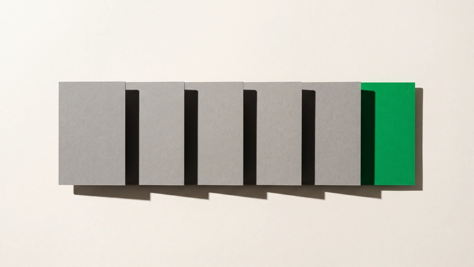 Six cartes rectangulaires alignées en rangée sur papier beige, vues du dessus, chacune chevauchant la précédente du même pas, cinq en carton gris et la dernière verte, ombres dures vers le bas à droite.