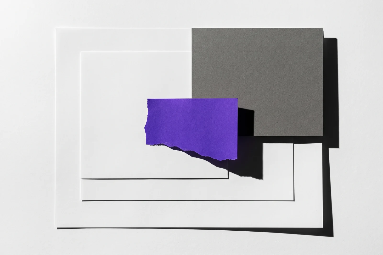 Des feuilles de papier fin collées en couches qui se recouvrent partiellement, ombres dures projetées vers le bas à droite.