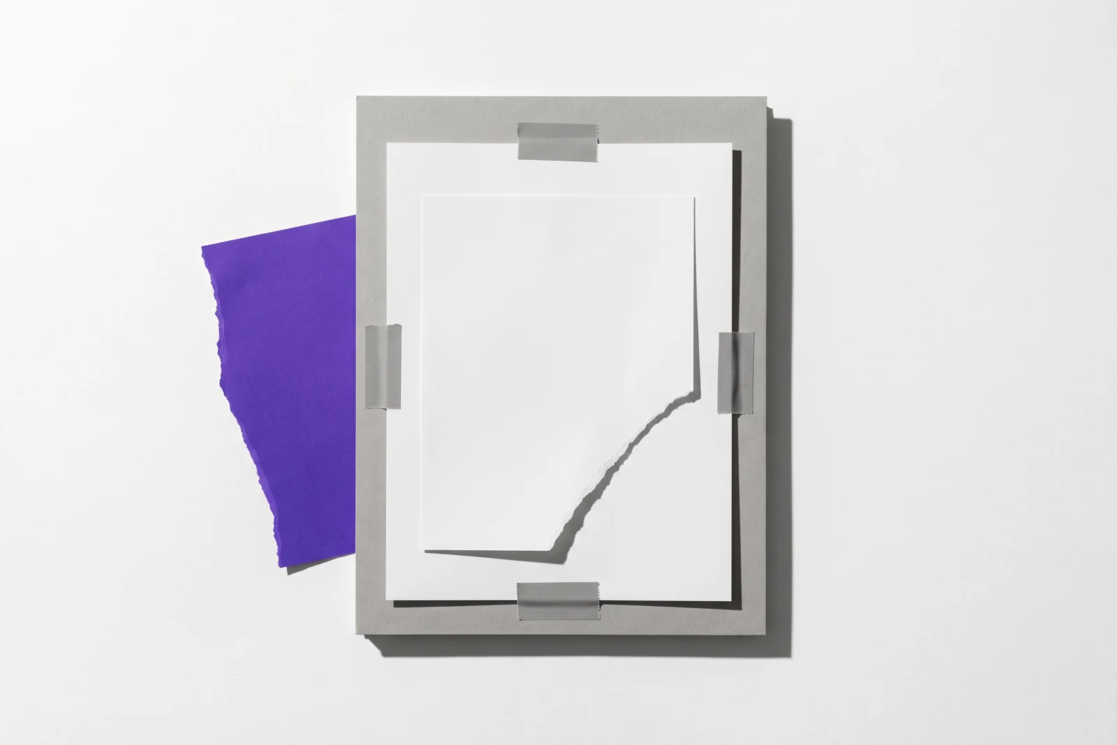 Des feuilles de papier scotchées à plat, le coin de la feuille du dessus arraché, ombres dures projetées vers le bas à droite.