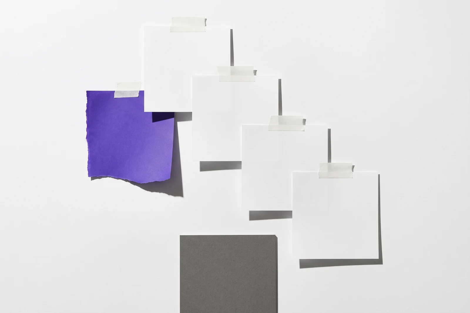 Des feuilles identiques scotchées en cascade à décalage constant, ombres dures projetées vers le bas à droite.