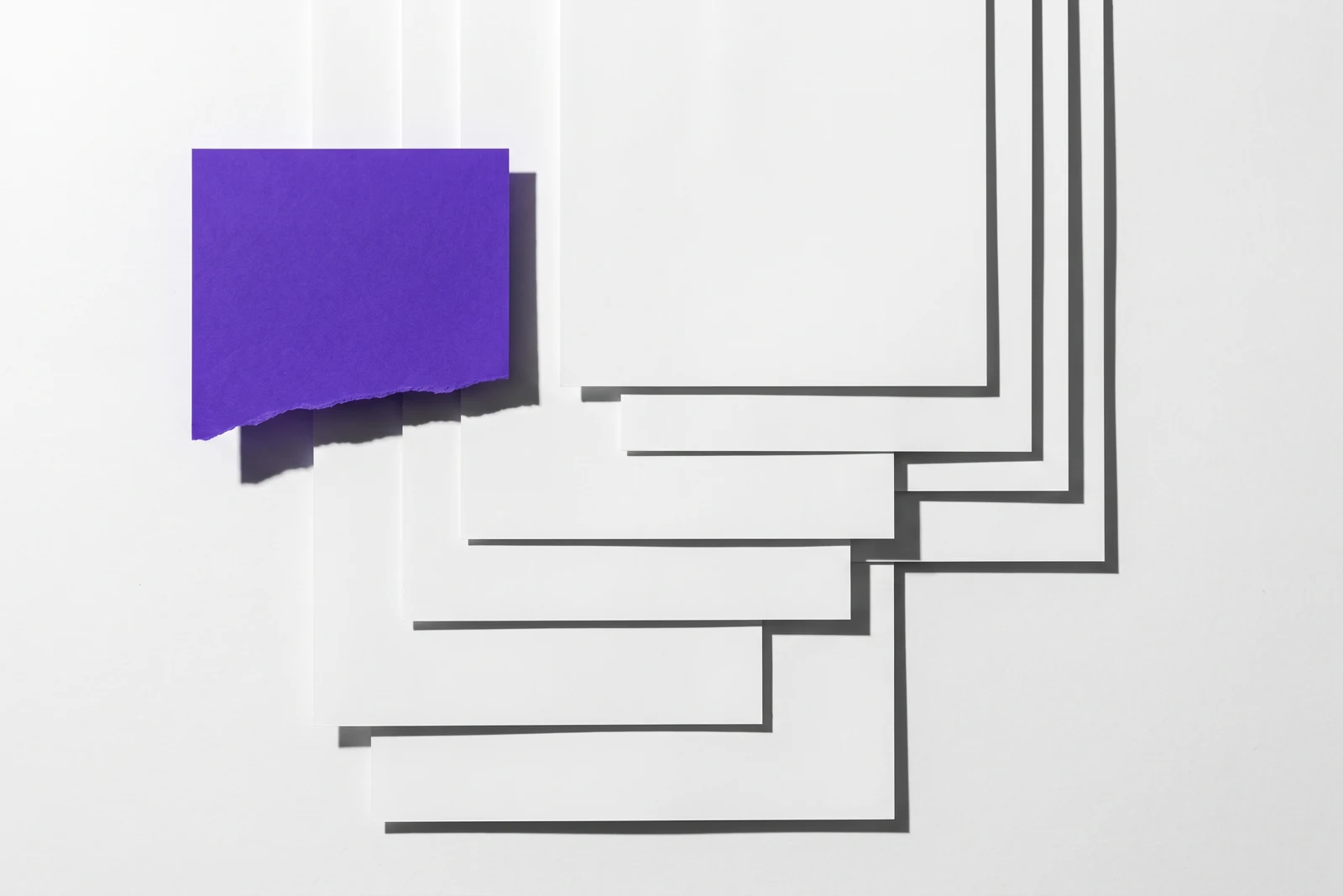 Des feuilles de papier fin collées en couches qui se recouvrent partiellement, ombres dures projetées vers le bas à droite.
