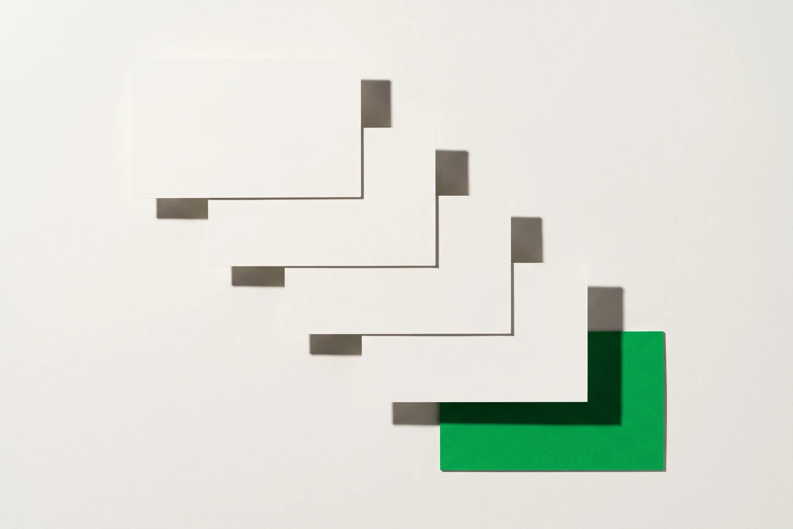 Cinq cartes de papier mat posées en escalier régulier descendant vers la droite, la dernière marche étant une carte de papier vert