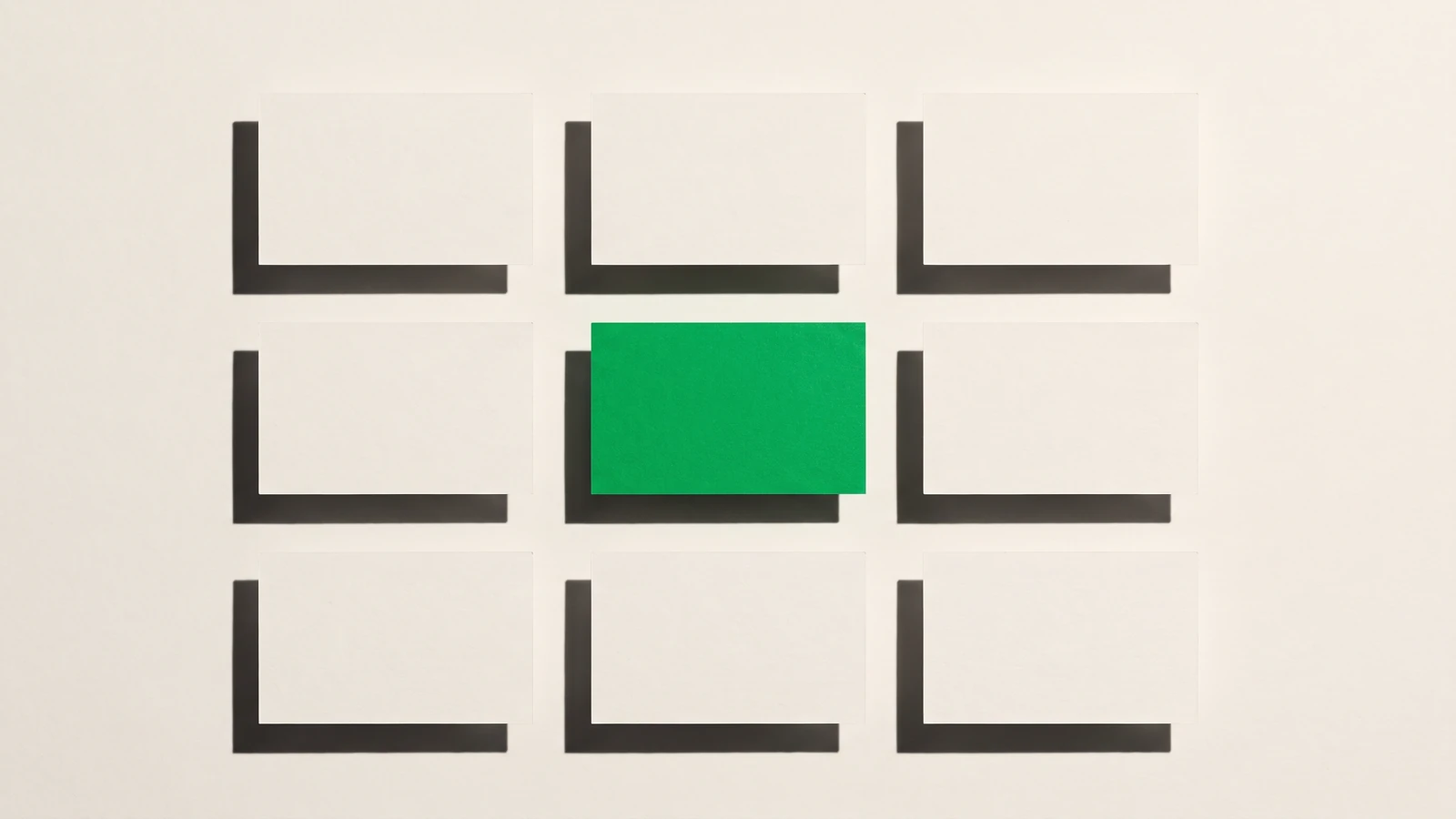 Neuf cartes de papier vierge disposées en trois colonnes régulières de trois, la carte centrale en papier vert, ombres dures projetées dans une seule direction