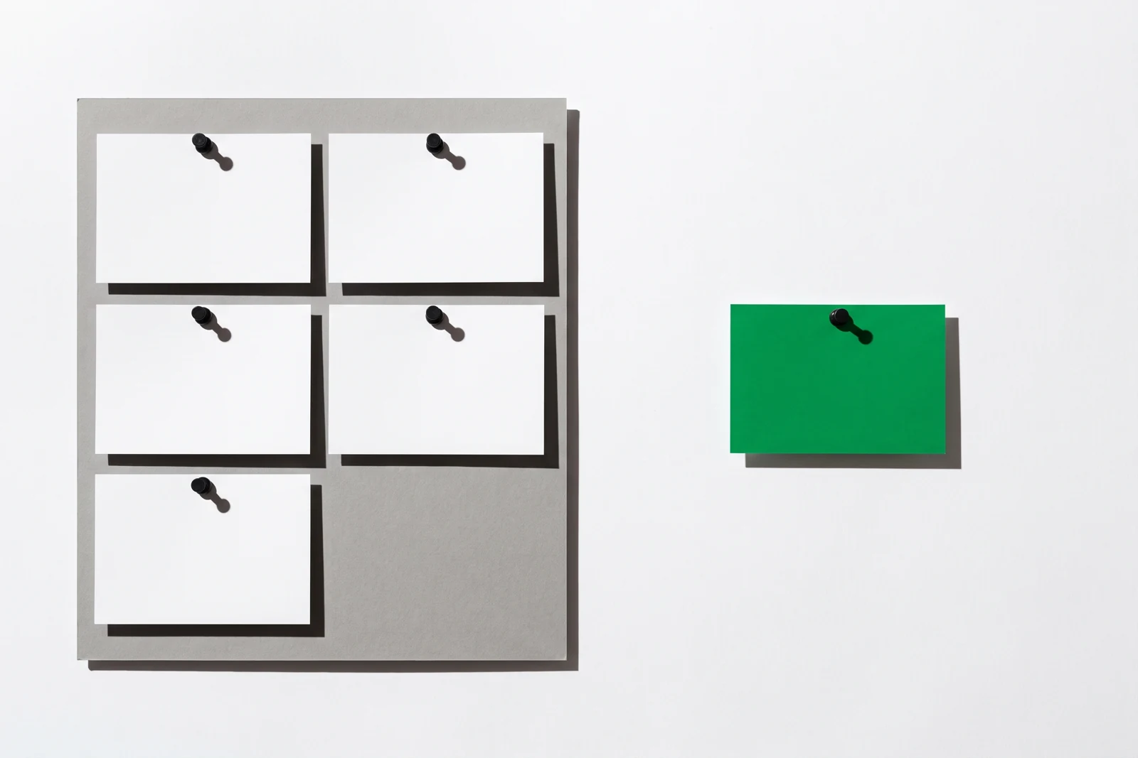 Cinq cartes blanches punaisées en bloc sur un carton gris avec une case laissée vide, et une carte verte punaisée seule à l'écart sur la droite.