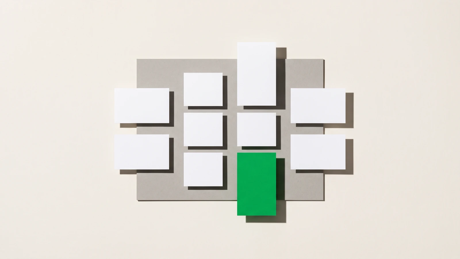 Des cartes de papier blanc vierge rangées en quatre colonnes sur une plaque de carton gris, une seule carte verte en bas de la troisième colonne, ombres dures projetées vers le bas à droite.