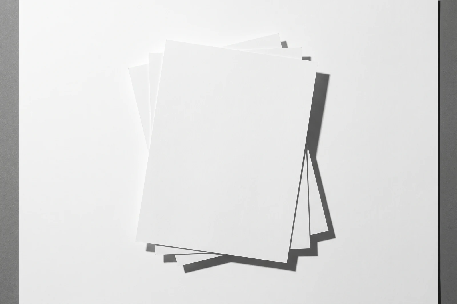 Des feuilles de papier fin empilées à plat et visiblement désalignées, ombres dures projetées vers le bas à droite.