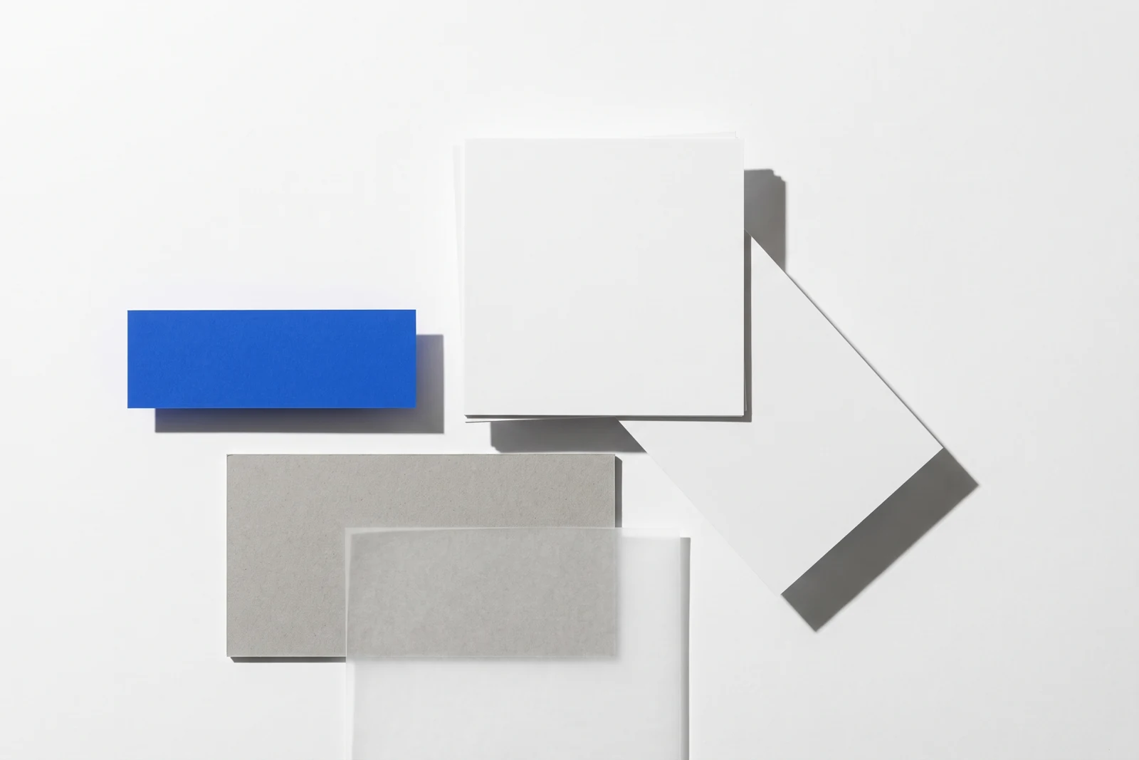 Une carte glissée hors d’une pile de papier vierge et qui dépasse nettement, ombres dures projetées vers le bas à droite.