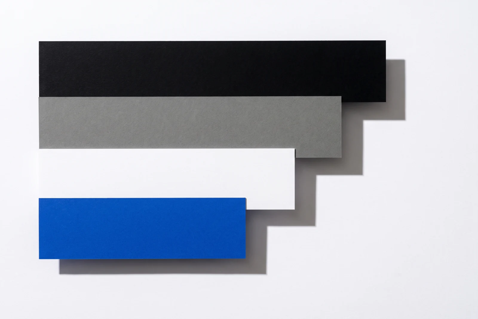 Des pièces de papier vierge disposées en escalier descendant, ombres dures projetées vers le bas à droite.