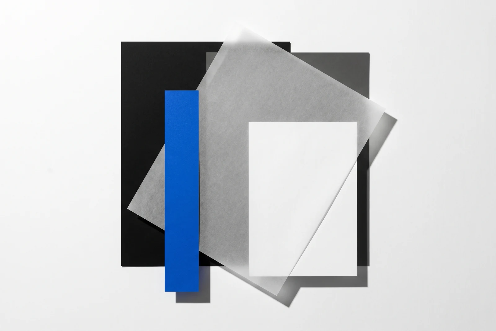 Un calque cristal posé de biais sur des feuilles de papier vierge, ombres dures projetées vers le bas à droite.