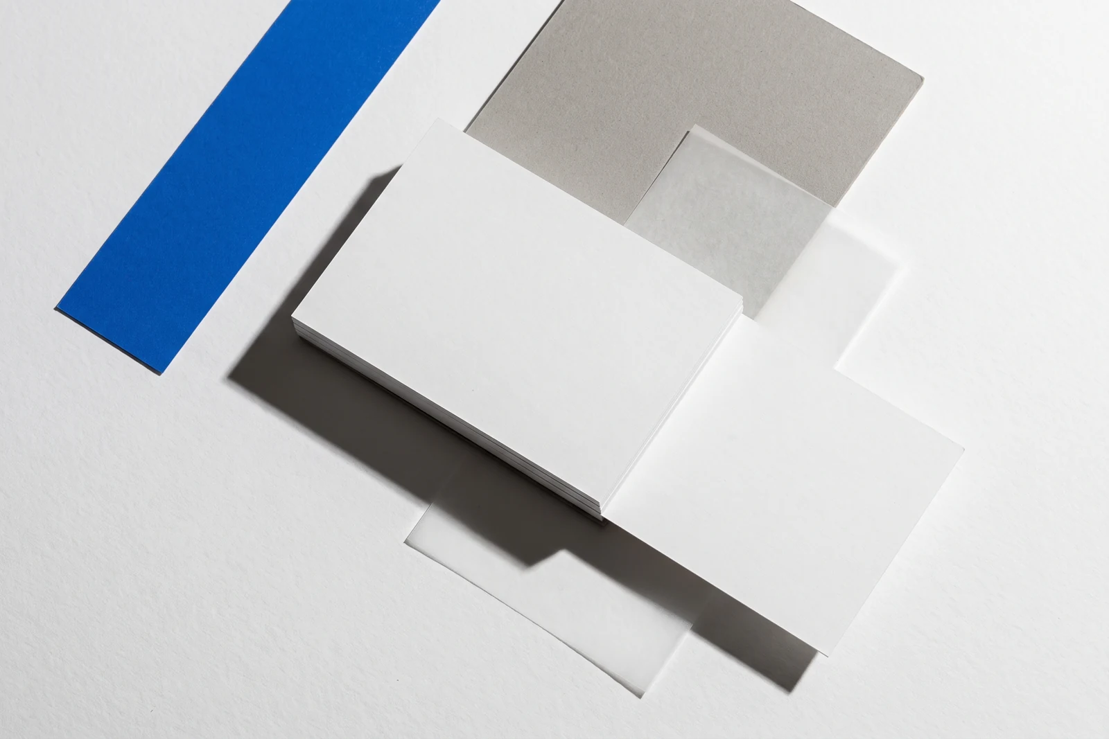 Une carte glissée hors d’une pile de papier vierge et qui dépasse nettement, ombres dures projetées vers le bas à droite.